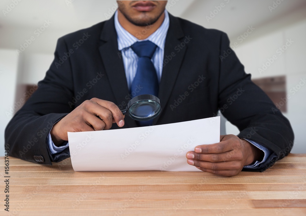 Man looking at paper with magnifying glass at desk