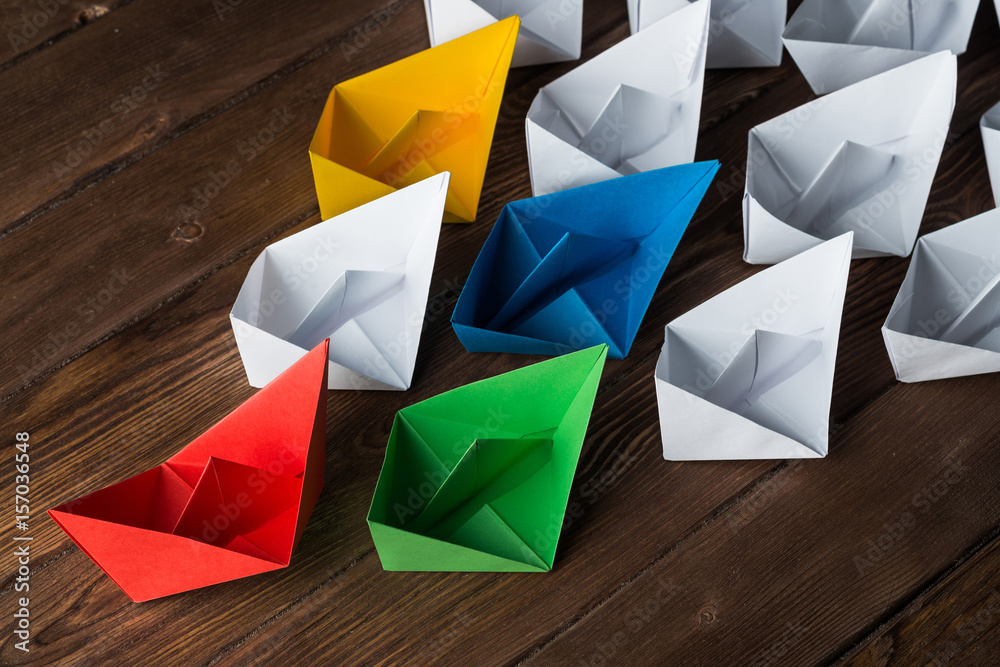 Business leadership concept with white and color paper boats on wooden table