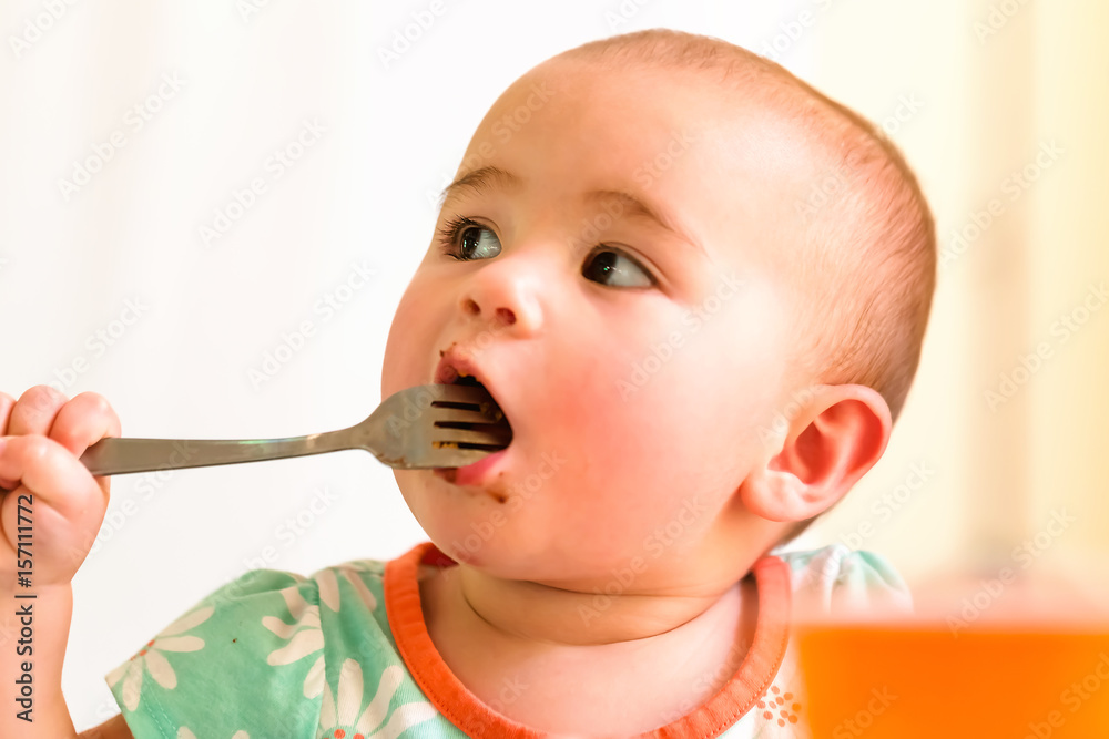 Toddler girl eating food with a fork