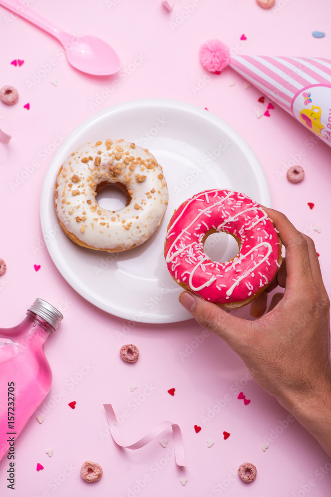 Party. Hand holding colourful sugary round glazed donuts and bottles of drinks on pink background.