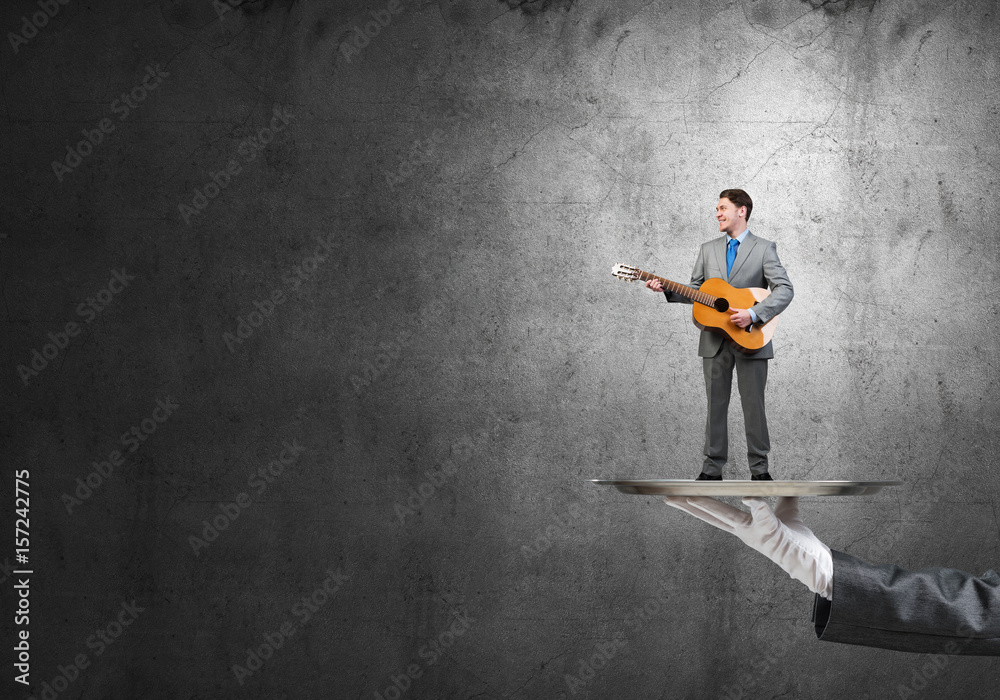 Businessman on metal tray playing acoustic guitar against concrete wall background