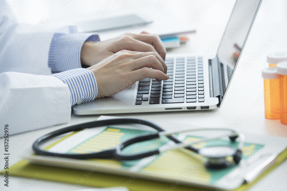 The doctor is working in a laptop in the medical office