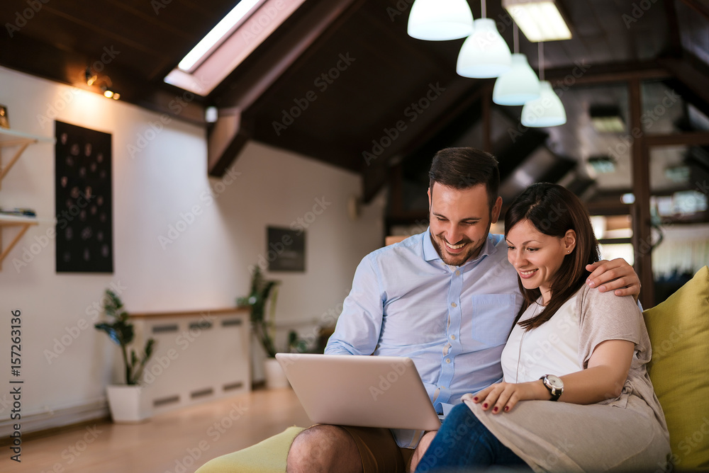 Young couple in love resting on the couch and surfing the web on a laptop computer.