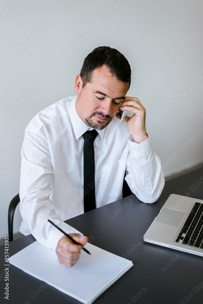 Entrepreneur working on the phone and writing notes sitting in a desk at office