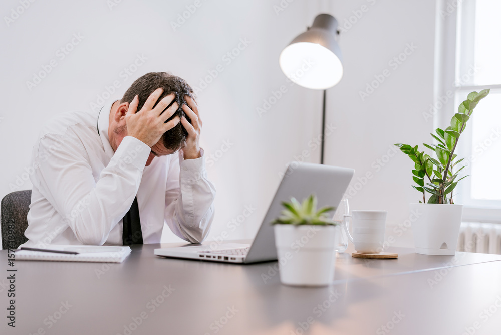 Frustrated middle aged businessman sitting at office desk