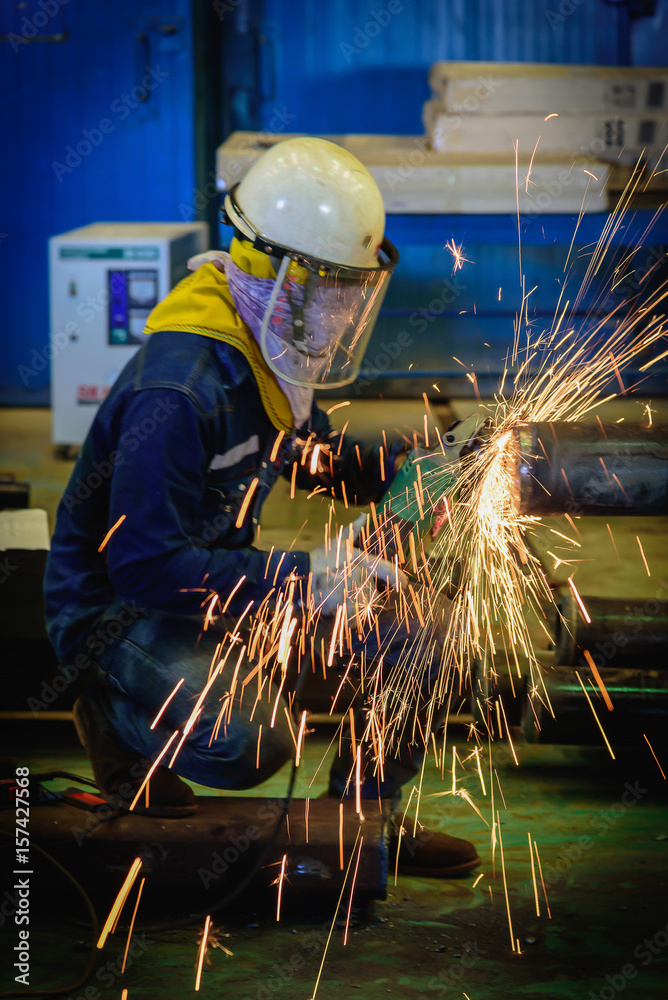 Heavy industrial worker used electric wheel grinding on steel pipe in steel factory with sparks.