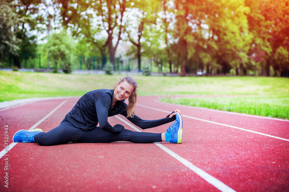 Athletic woman stretching on running track before training, healthy lifestyle