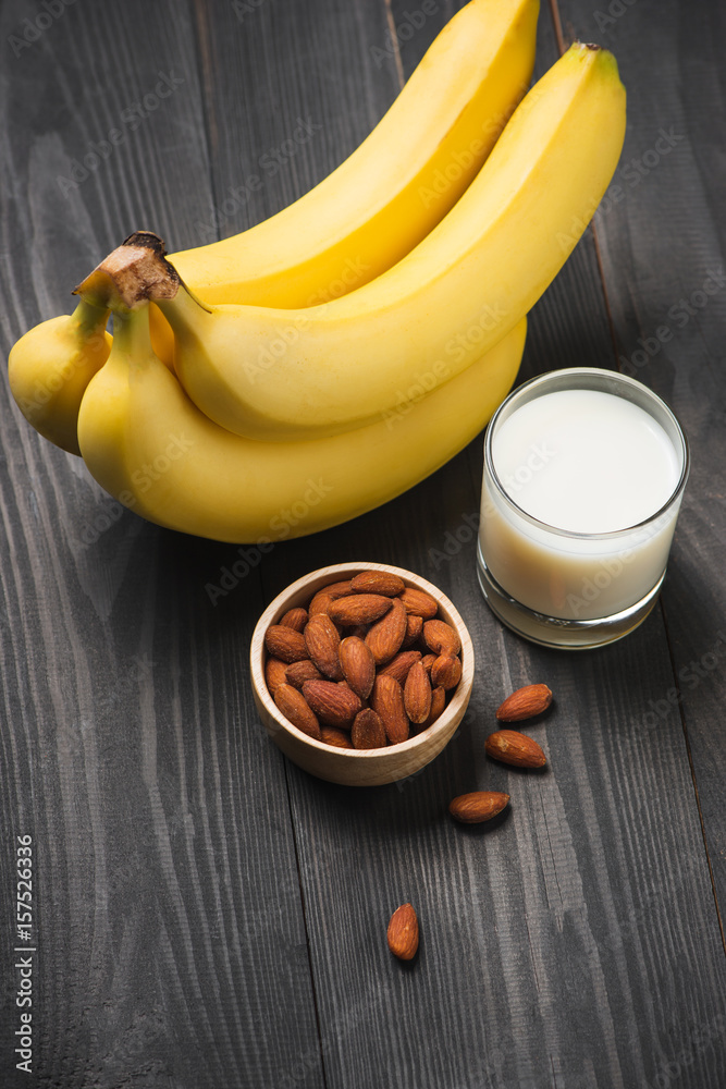 A banch of bananas with almonds and milk on wooden background.