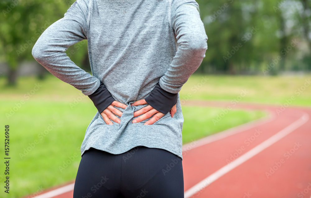 Athletic woman on running track touching hurt back with painful injury