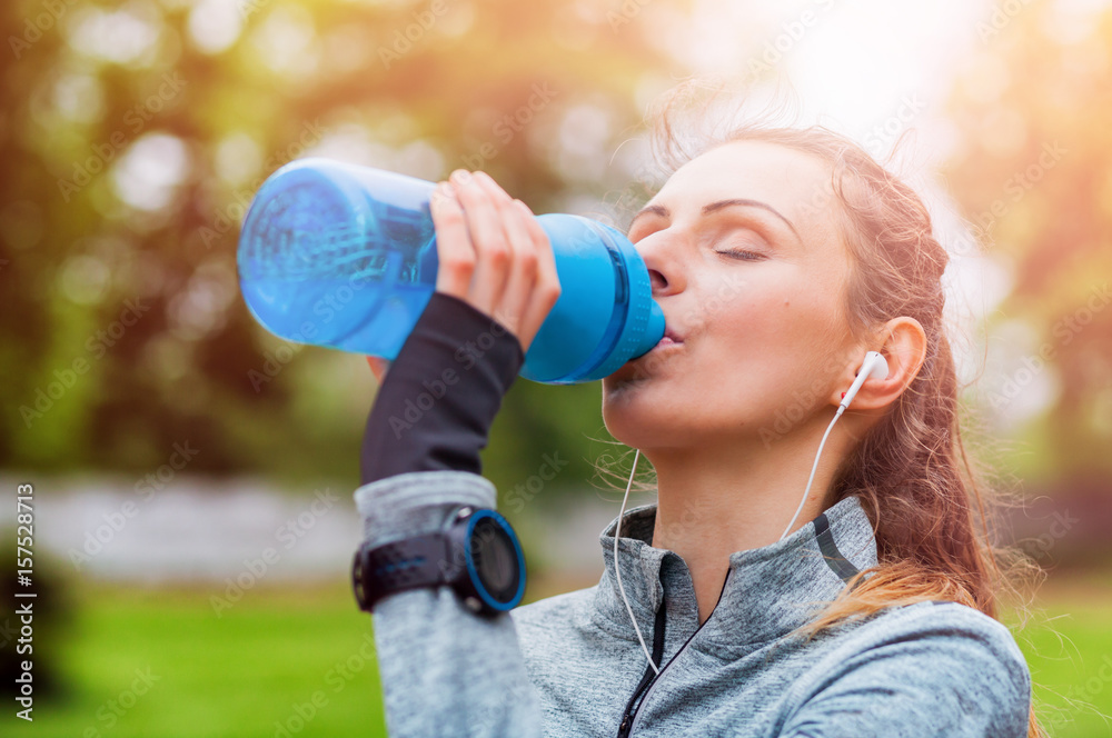 Athletic woman after running workout drinking water fitness accessories