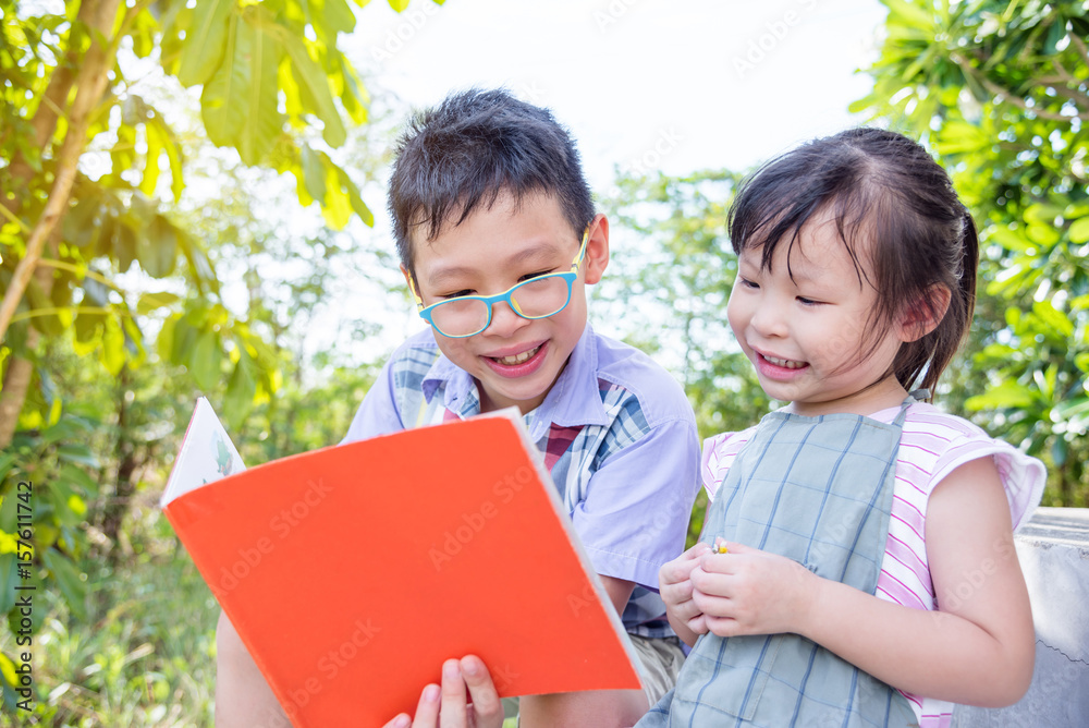 Young asian boy reading a story to his sister in park