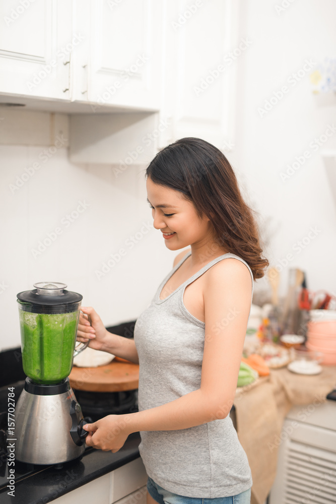 微笑的亚洲女人在家里厨房的搅拌机里用新鲜蔬菜做奶昔。