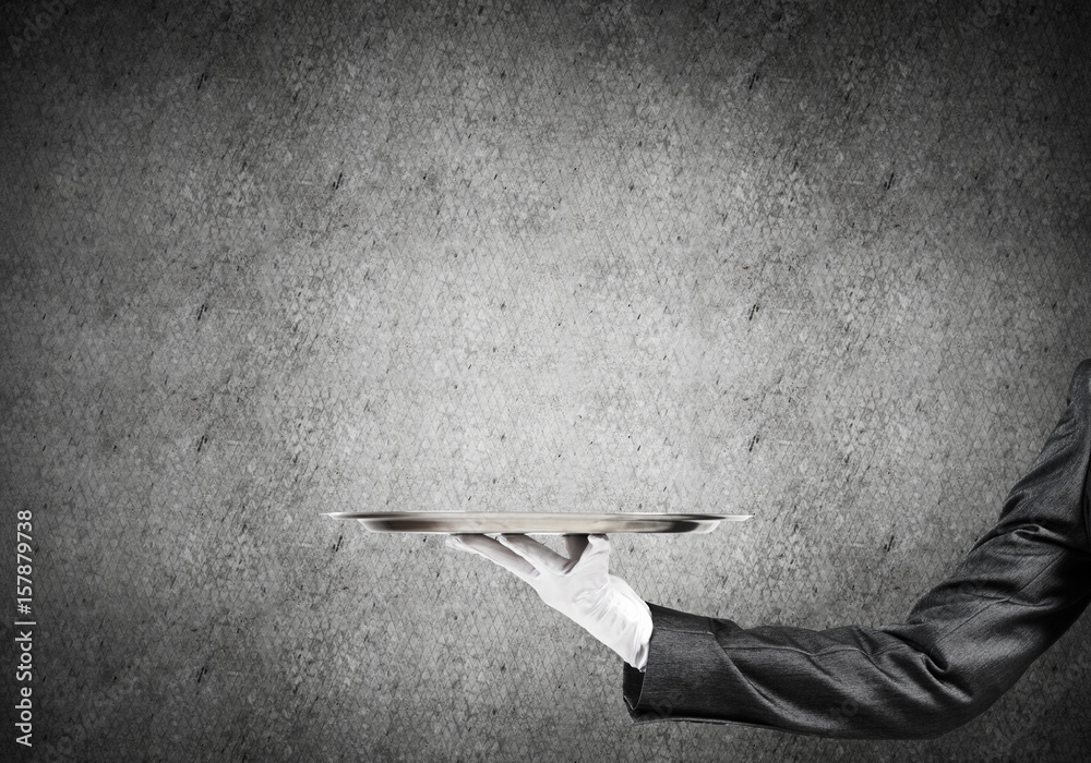 Hand of butler holding empty metal tray against concrete background