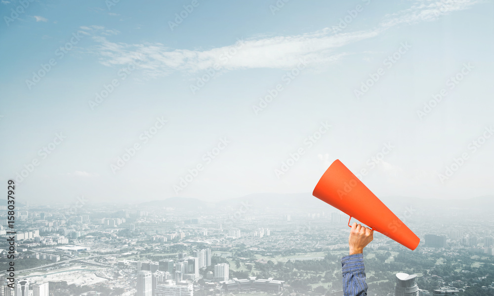 Hand of man holding red paper trumpet against cityscape background