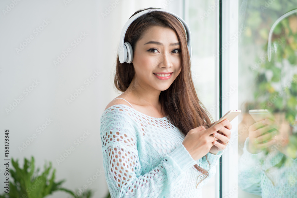 Asian woman enjoying view on windowsill and listening to music.