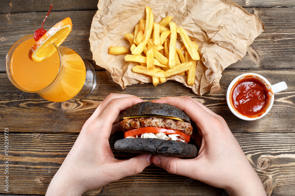 Hands holding fresh delicious burgers with french fries, sauce and fresh orange juice or alcoholic c