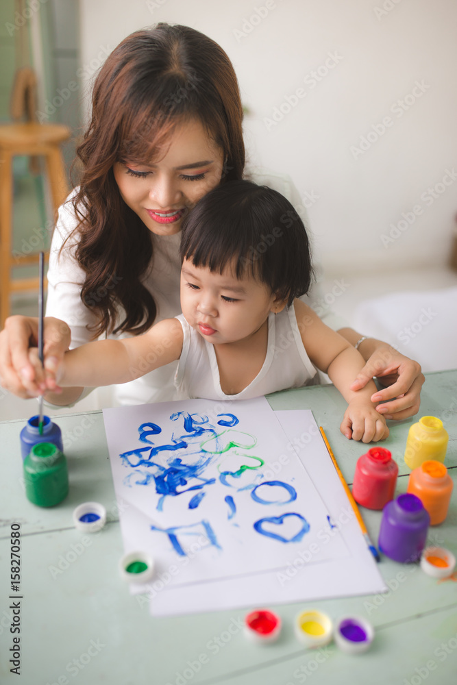 幸福的家庭，母亲和女儿一起画画。亚洲妇女帮助她的小女儿。