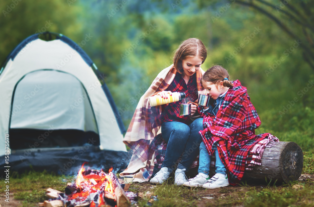 Family mother and child daughter drinking tea on a camping trip with a tent