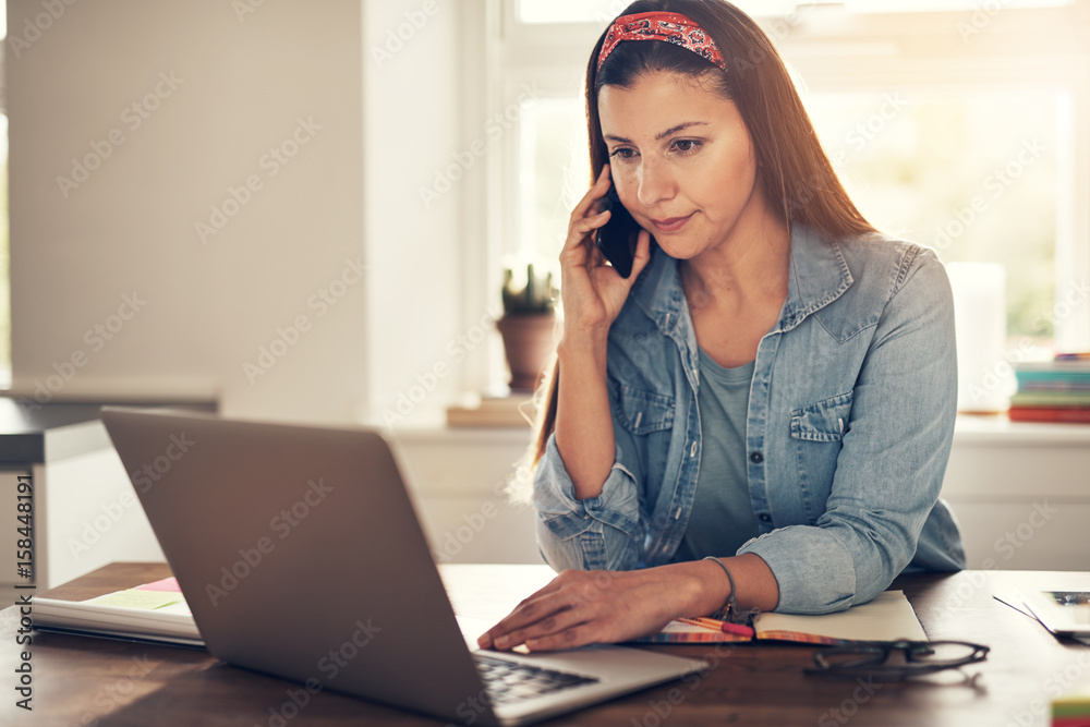 Young businesswoman talking smartphone and browsing laptop