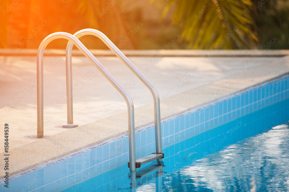 Grab bars ladder in the blue swimming pool with Orange sun light in mornung