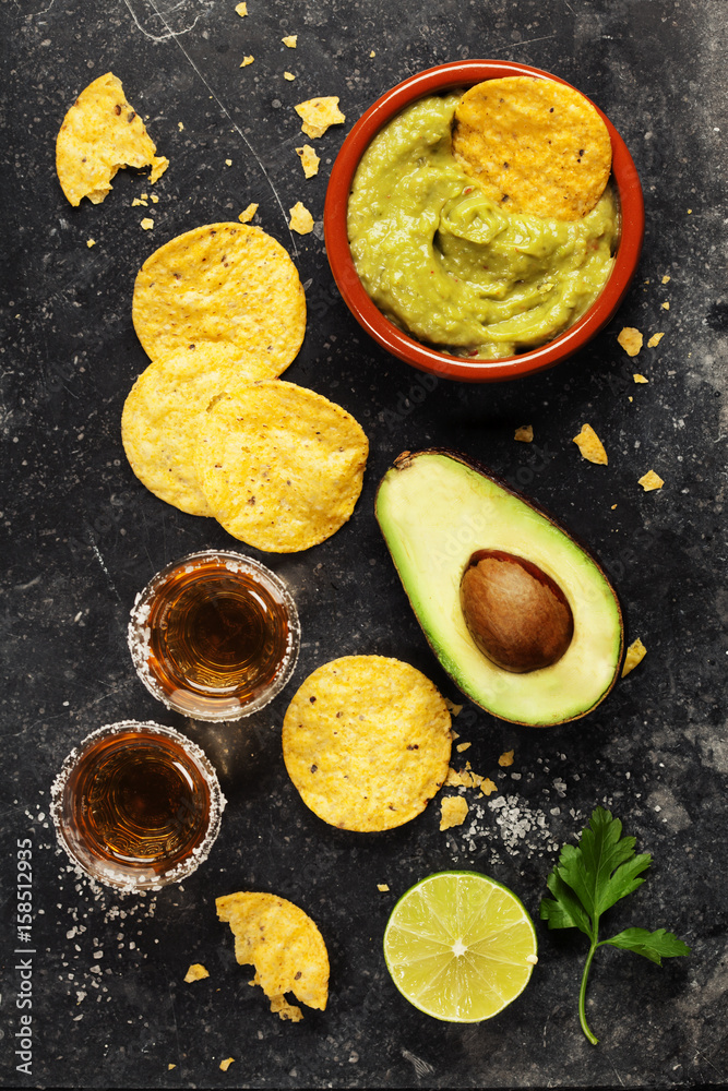 Bowl of mexican nachos chips with homemade fresh guacomole sauce and tequila shots