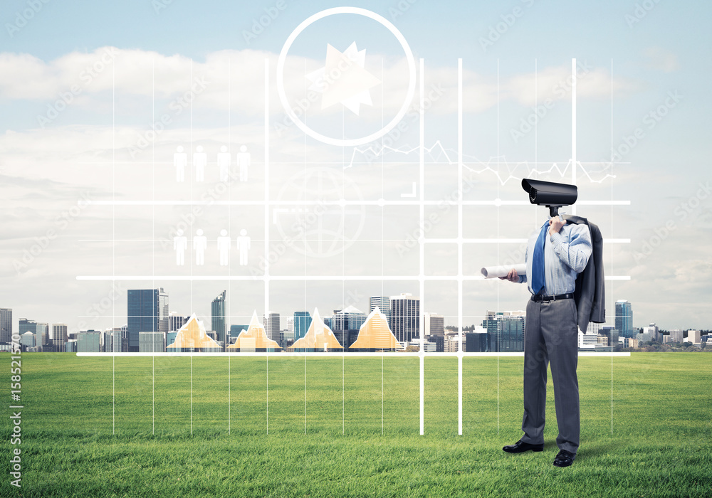 Camera headed man standing on green grass against modern citysca