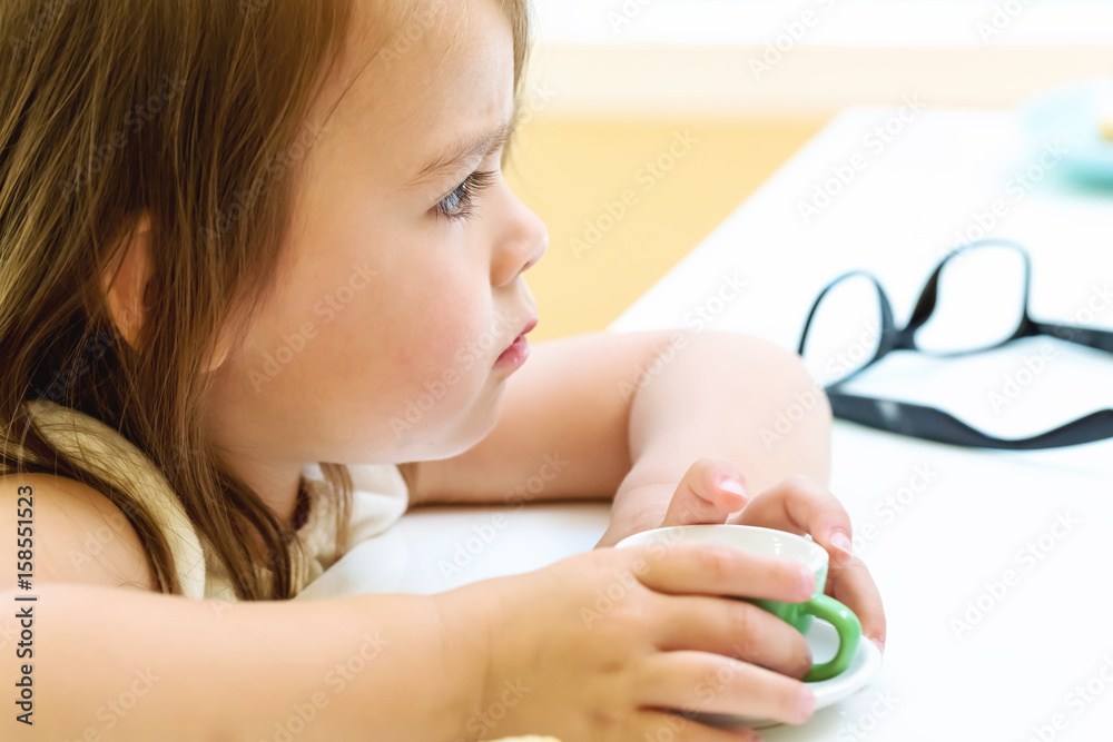 Toddler girl with tiny teacup at a desk