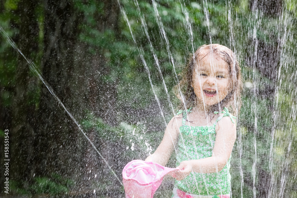 Happy toddler girl playing in a sprinkler