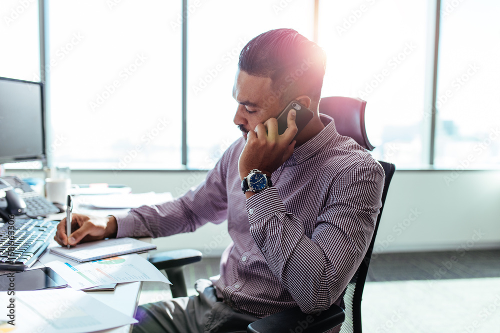 Businessman talking over mobile phone sitting at his office desk