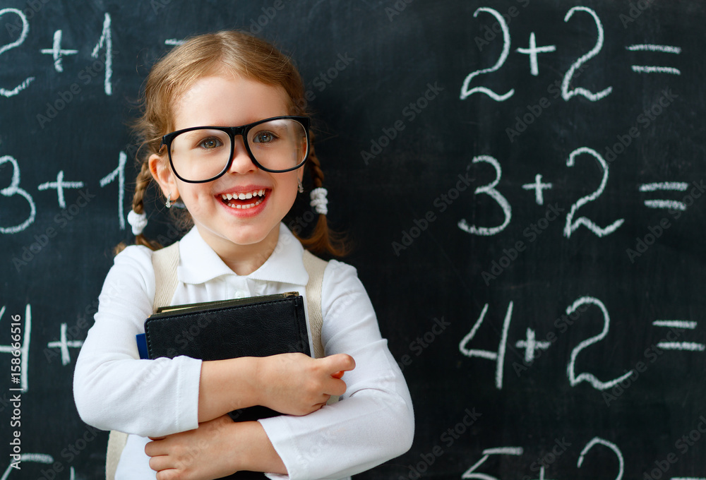 Happy schoolgirl preschool girl with book near school blackboard