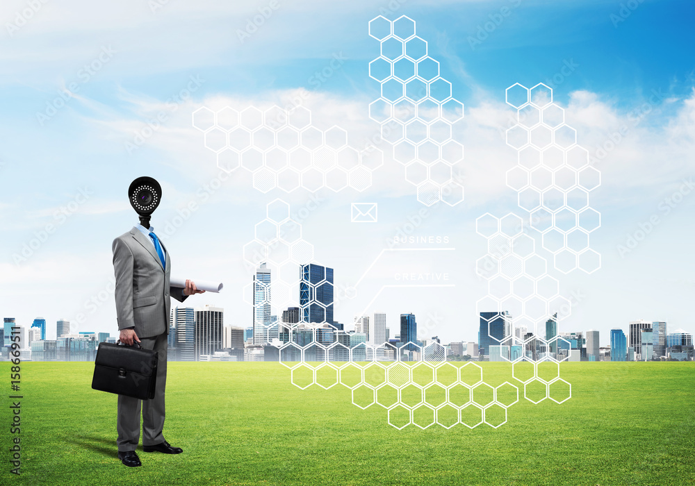 Camera headed man standing on green grass against modern cityscape