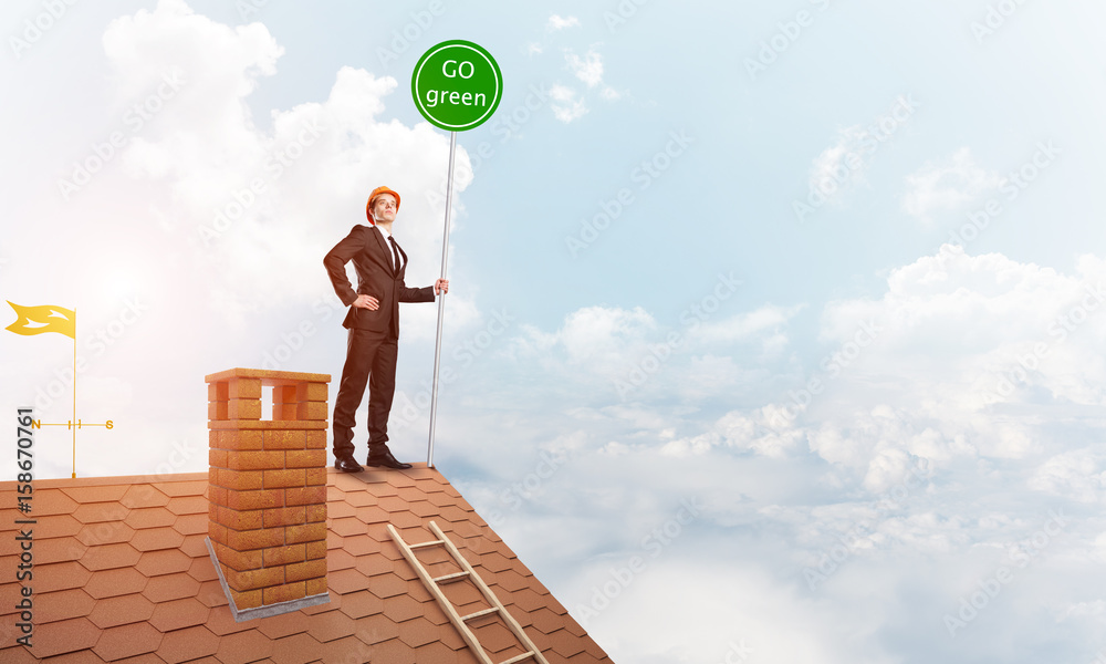 Businessman in suit on house top with ecology concept signboard. Mixed media