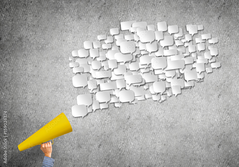 Hand of man holding yellow paper trumpet against concrete background