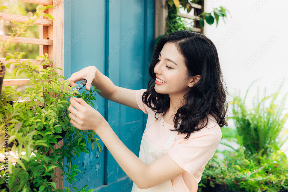 花园里穿着围裙的年轻职业女性修剪绿色灌木