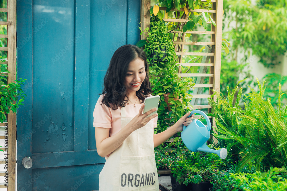 年轻的亚洲女性使用智能手机，一边给植物浇水一边在手机上打字