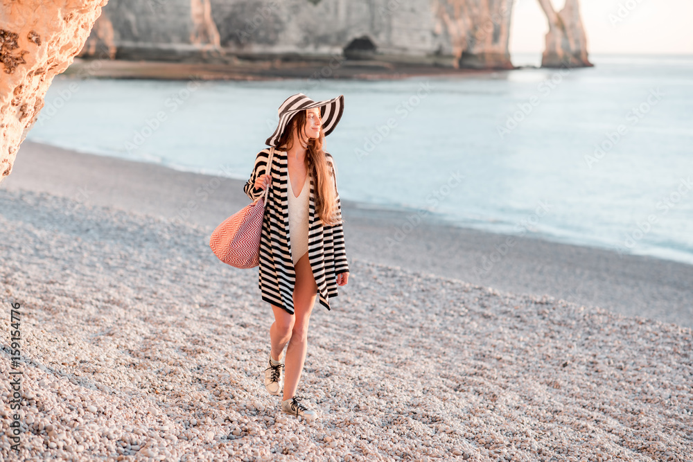 Woman in striped sweater and hat walking on the beach during the summer evening