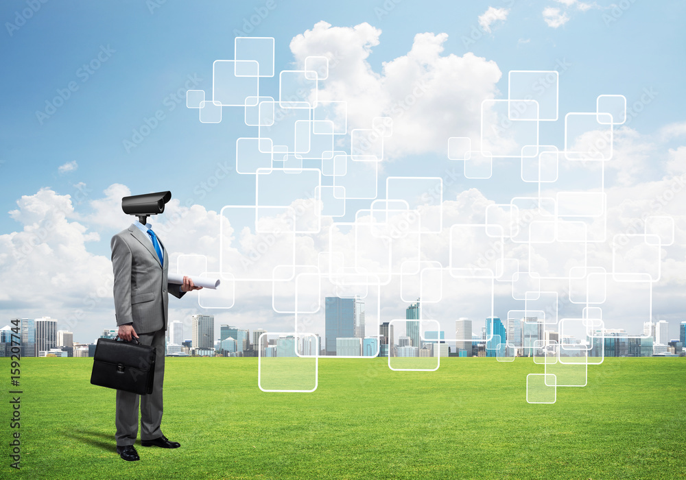 Camera headed man standing on green grass against modern cityscape