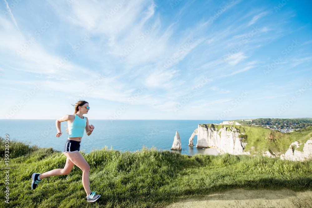 Young woman in sportswear running outdoors on the beautiful rocky coastline with great view on the o