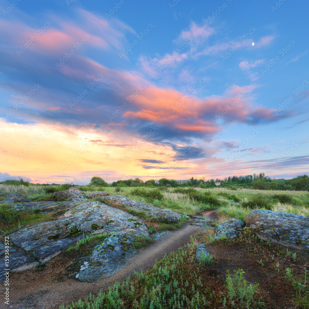 Colorful summer landscape with big stones, green grass, walkway and amazing sky with multicolored cl