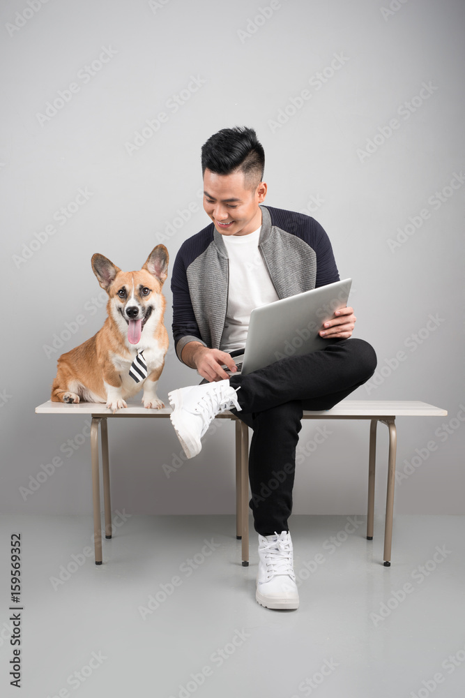 Handsome young businessman is using laptop while sitting with his dog o chair