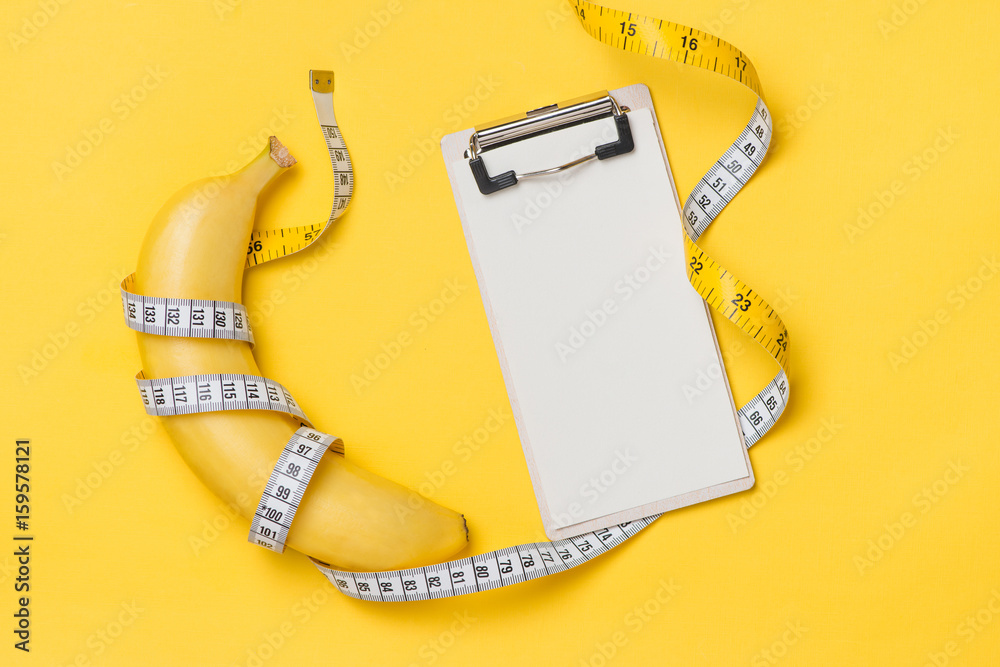 Diet, fitness and health concept presented by yellow banana wrapped in measure tape isolated on yell