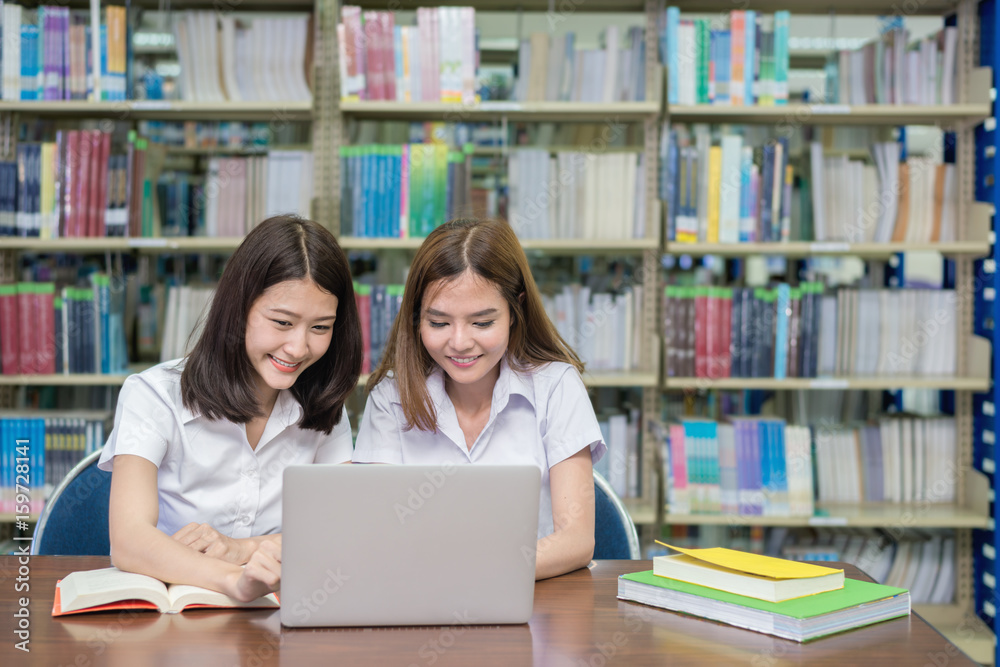 亚洲快乐学生带着笔记本电脑在图书馆工作和学习。人、教育、技术