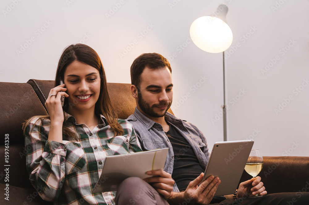 Couple sitting on couch with tablet and phone, woman talking on phone