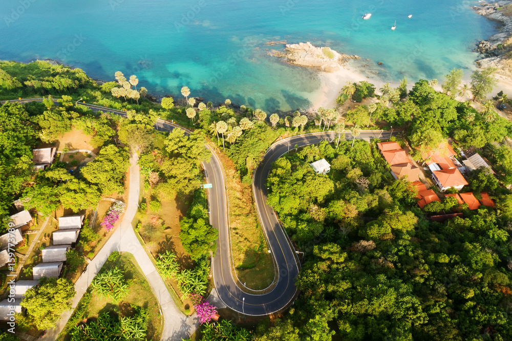 Aerial shot of sunrise landscape, serpentine road, bay with clear turquoise water and ychts on horiz