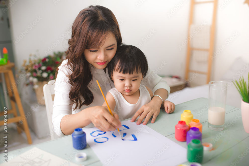 幸福的家庭，母亲和女儿一起画画。一位亚洲妇女帮助她的小女儿。