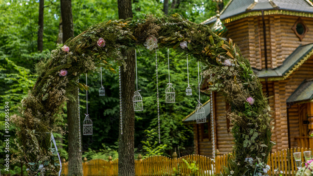 Arch for the wedding ceremony. Decorated with fabric flowers and greenery. Is located in a pine fore