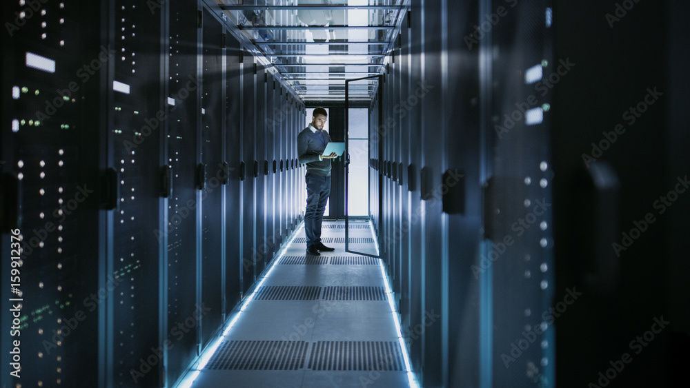 Long Shot of IT Technician Works on Laptop in Big Data Center full of Rack Servers. He Runs Diagnost