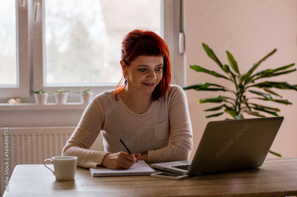 Happy student learning on line and taking notes in a notepad