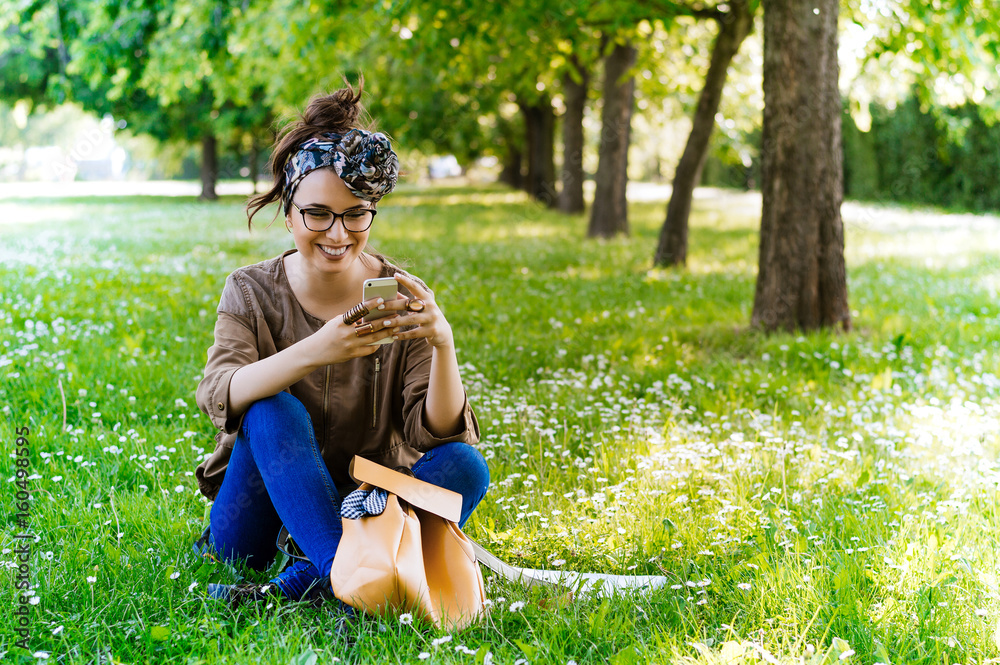 Break time. Young woman using cellphone and sitting on the grass.