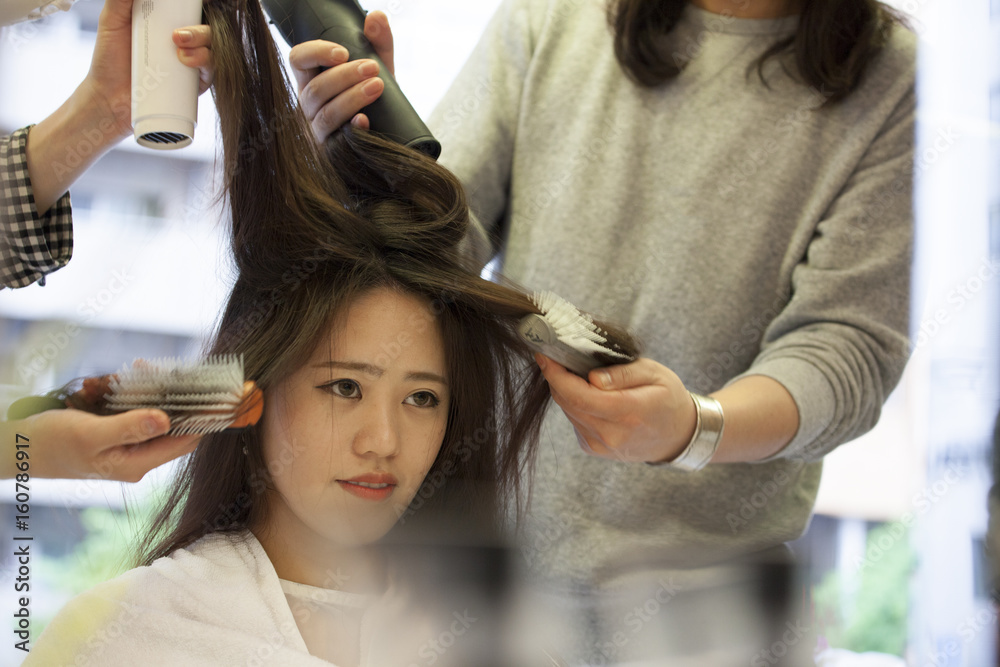 Two hairdressers are drying the womens hair with a hair dryer